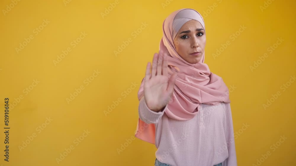 Stop hand. No gesture. Risk prevention. Rejecting serious woman in hijab showing outstretched palm in refusal sign isolated on yellow empty space studio background. Stop hand. No gesture. Risk prevention. Rejecting serious woman in hijab showing outstretched palm in refusal sign isolated on yellow empty space studio background.