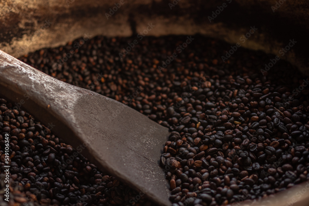 Coffee beans, roasted coffee beans are mixed with a spatula. Coffee plantation, stages of coffee processing Coffee beans, roasted coffee beans are mixed with a spatula. Coffee plantation, stages of coffee processing