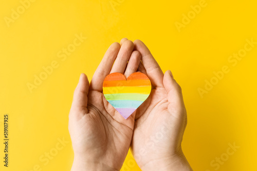 International Day Against Homophobia, Transphobia and Biphobia. May 17. Stop Homophobia. Heart with rainbow LGBT flag in hands on yellow background.