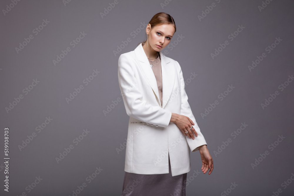 Fashion photo of a beautiful elegant young woman in a pretty white jacket, long metallic silver platinum skirt, sneakers posing gray background. Studio Shot. Portrait Fashion photo of a beautiful elegant young woman in a pretty white jacket, long metallic silver platinum skirt, sneakers posing gray background. Studio Shot. Portrait