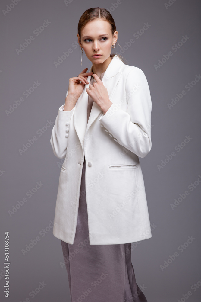 Fashion photo of a beautiful elegant young woman in a pretty white jacket, long metallic silver platinum skirt, sneakers posing gray background. Studio Shot. Portrait Fashion photo of a beautiful elegant young woman in a pretty white jacket, long metallic silver platinum skirt, sneakers posing gray background. Studio Shot. Portrait