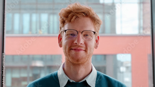 Young ginger irish man in glasses smiling with pleased happy expression and looking at camera portrait. Millennial male freelancer successful entrepreneur,young businessman standing in office. Slow mo photo