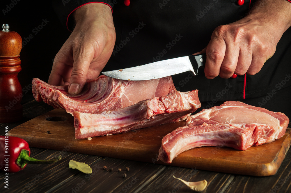 Chef cuts raw ribs on a cutting board before baking. Cooking delicious food in the kitchen