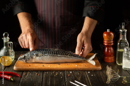 Fish Chef prepares mackerel or Scomber in the hotel kitchen. The concept of cooking fish on a dark background. European cuisine