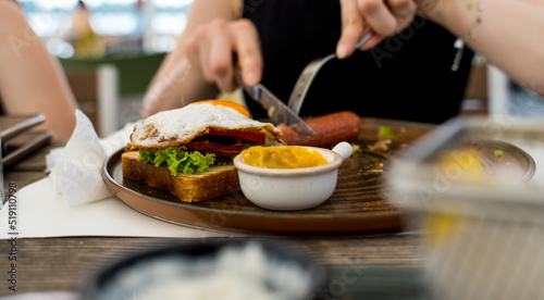 A close up girl is eating healthy English breakfast during the day in a restaurant cutting sausage and sandwich 