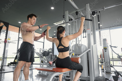 A young Asian bodybuilder trainer is teaching Asian women the correct use of exercise equipment in the gym. Young Asian male trainer is teaching Asian girls the right exercises in the gym.