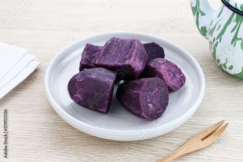 Steamed Purple Sweet Potato (Ubi ungu kukus) served in white plate on wooden table. 