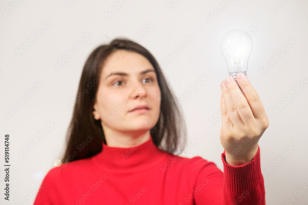A surprised brunette woman with her mouth open in red looks at a glowing light bulb, surprise and epiphany. New creative ideas, innovative technologies. A surprised brunette woman with her mouth open in red looks at a glowing light bulb, surprise and epiphany. New creative ideas, innovative technologies.