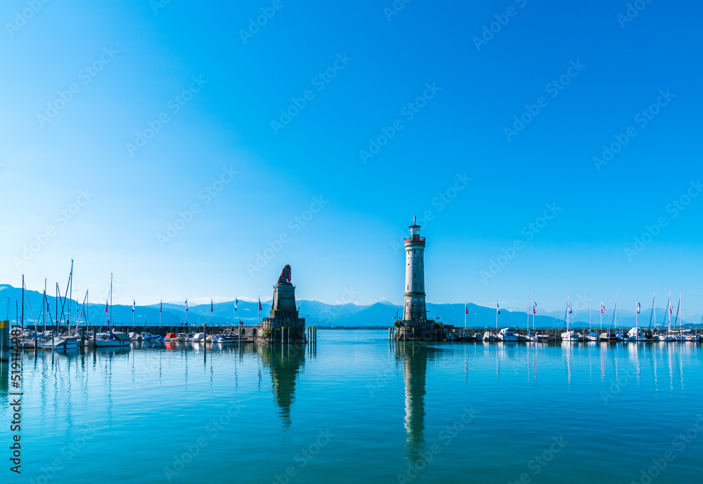 Germany, Lindau island city port lighthouse and beautiful panorama view to austria and bregenz city early in the morning with blue sky and sun