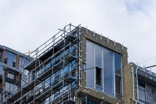 Construction work is underway in a new residential multi-storey brick and concrete block apartment building, around which scaffolding has been installed to provide access for outdoor work