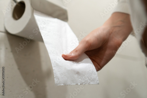Woman in a white coat sits on the toilet and pulls toilet paper in the bathroom. Selective focus