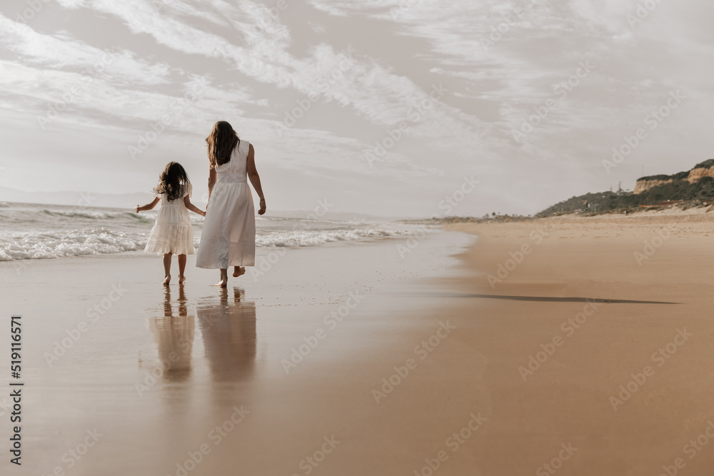 Anonymous female with little kid holding hands and walking on beach Anonymous female with little kid holding hands and walking on beach