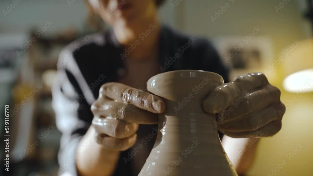 Young female potter gently pulls the neck of a clay vessel on a potter's wheel