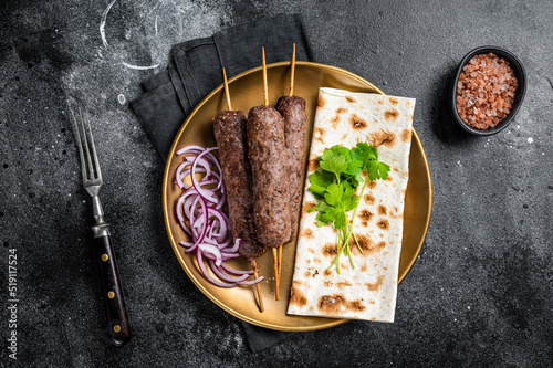 Lamb meat kofta kebab, onion and flat bread on plate. Black background. Top view photo