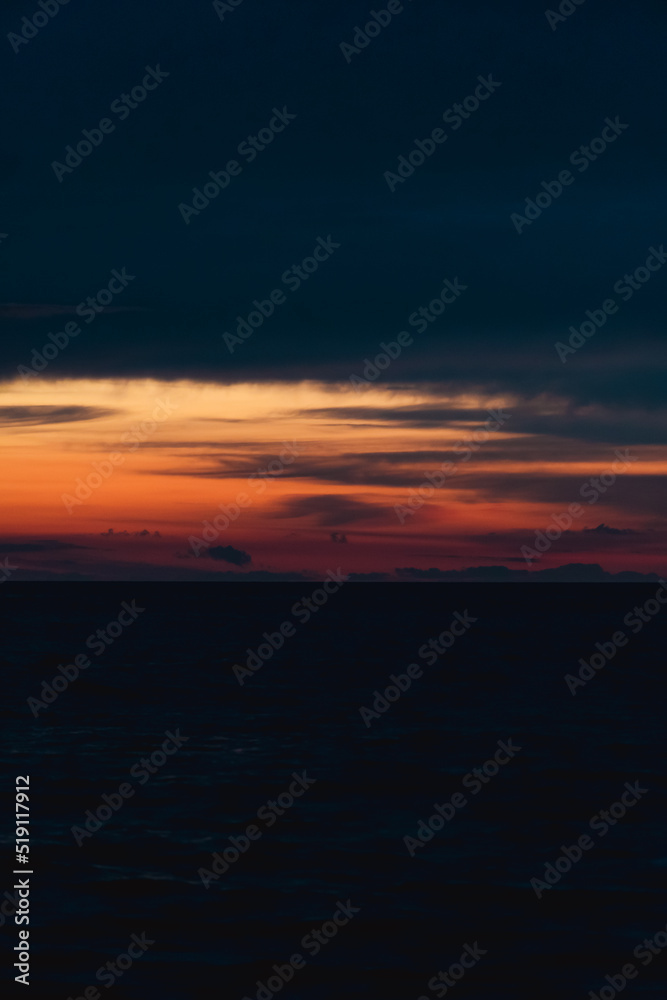 Dark sunset on the sea with orange flashes of light. Vertical photo