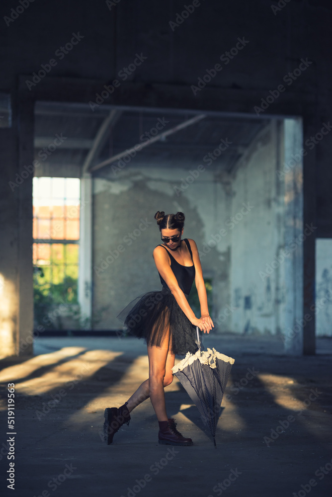 Goth ballerina holding umbrella and wearing sunglasses posing in abandoned building