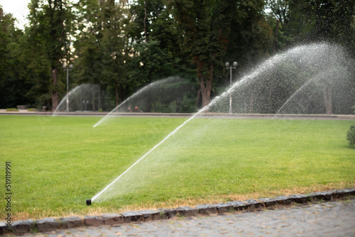 On green lawn, in a park or garden, a sprinkler is working. Automatic sprinkler irrigation system or device for watering of lawn. Grass irrigation. Garden Irrigation sprinkler watering lawn. Spraying 