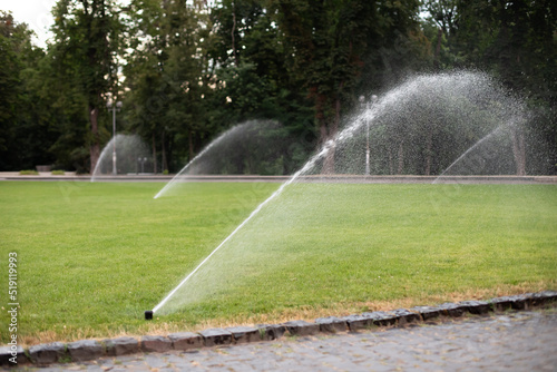 On green lawn, in a park or garden, a sprinkler is working. Automatic sprinkler irrigation system or device for watering of lawn. Grass irrigation. Garden Irrigation sprinkler watering lawn. Spraying 