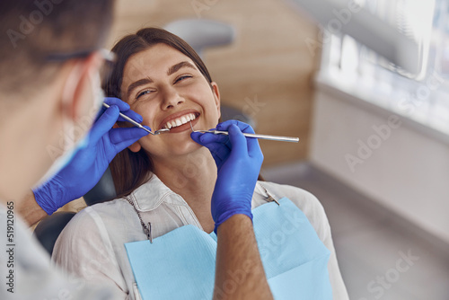 Professional doctor is checking woman's teeth in light modern dental clinic