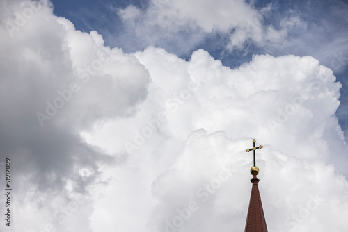Tower of the roof of a lutheran church with a cross on the very top with beautiful thick clouds in the background Nr.1