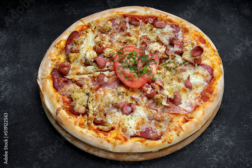 Pizza with meat sausage and chicken, cheese and tomatoes on a gray concrete background, with selective focus
