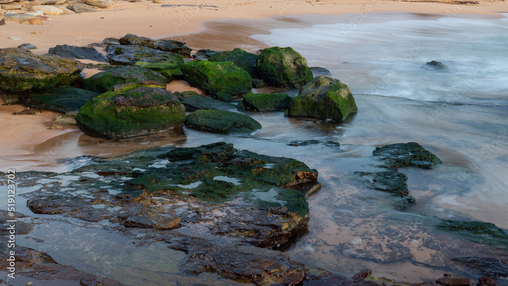 Rocks covered by green moss on the beach shore.