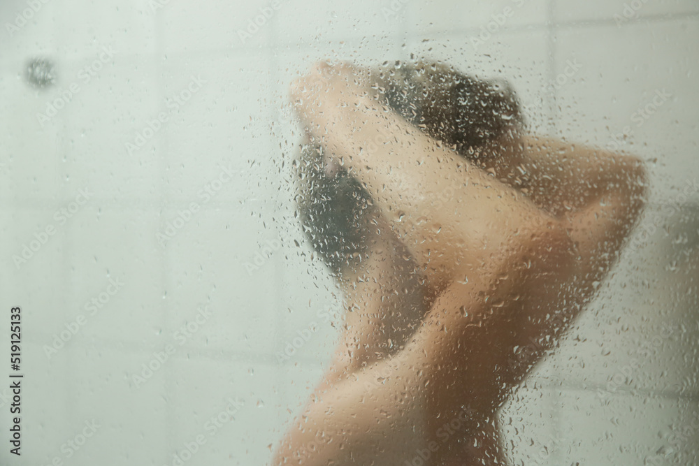 Young woman taking shower and washing her hair in shower cabine.