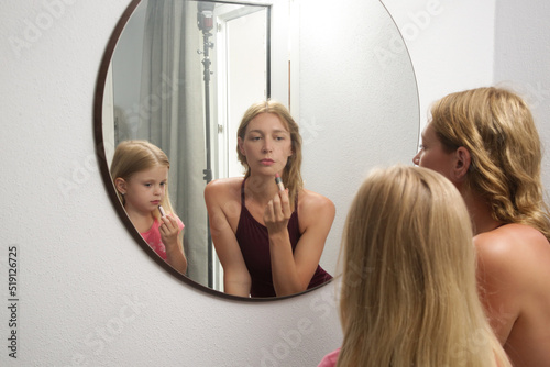 Mother and daughter applying lipstick in front of mirror