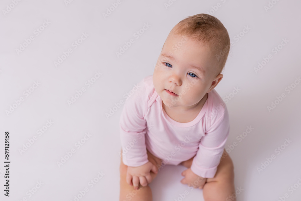 baby in a pink bodysuit is sitting on the floor, top view. baby in a pink bodysuit is sitting on the floor, top view.
