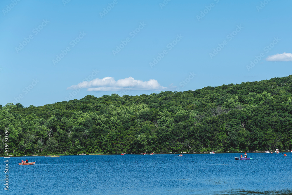 People on kayaks and canoe on lake, forest in the background and blue sky, sunny summer day. High-quality photo