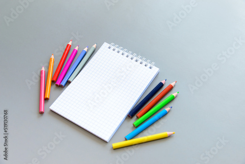 white blank opened notebook and school supplies on a gray background. White sheet of paper, colored pencils, felt-tip pens. Back to school