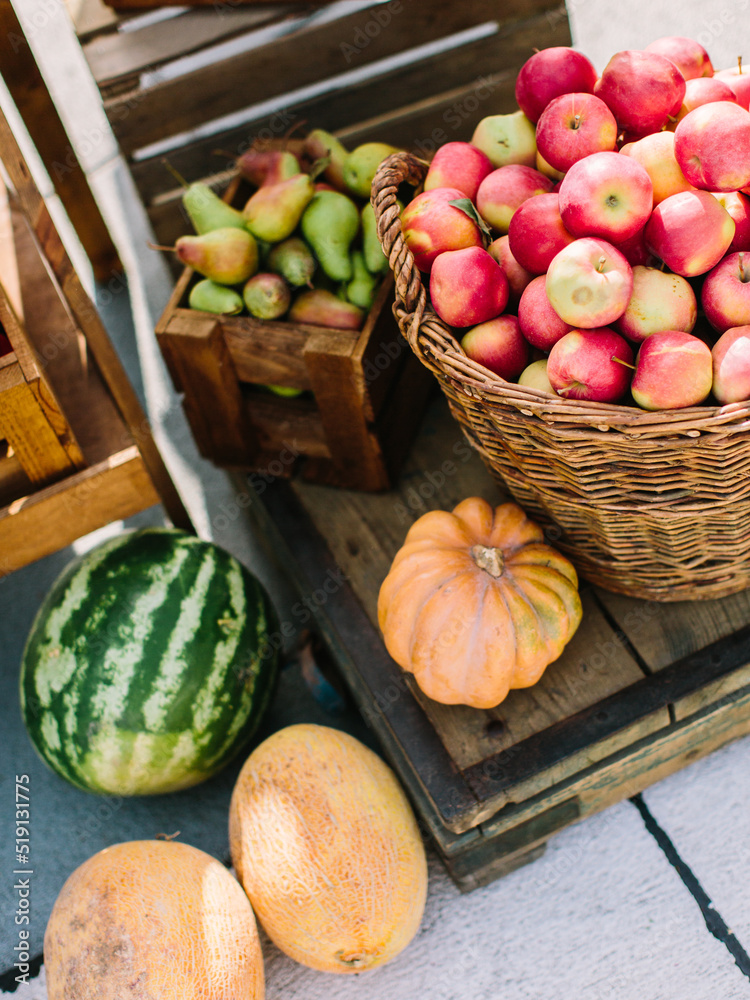 Vegetables at the street market: red apples in a wicker basket, pears in a wooden box, pumpkin, melons, ripe watermelon.