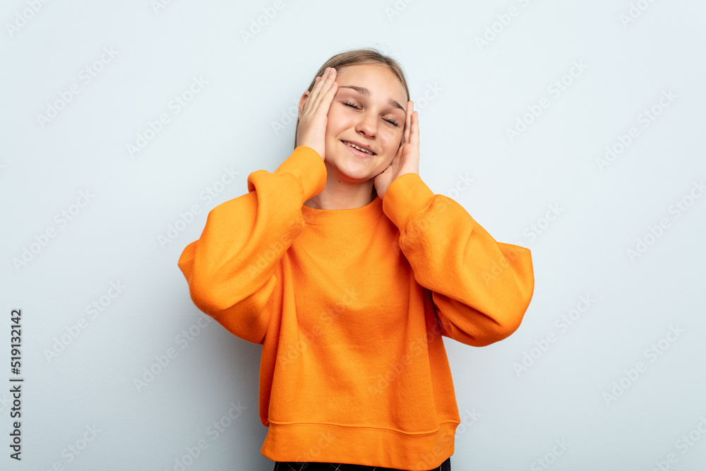 Young caucasian girl isolated on blue background laughs joyfully keeping hands on head. Happiness concept.