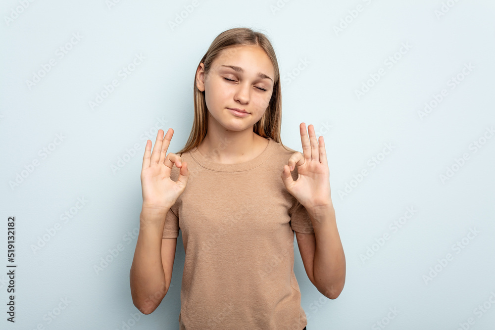 Young caucasian girl isolated on blue background relaxes after hard working day, she is performing yoga. Young caucasian girl isolated on blue background relaxes after hard working day, she is performing yoga.