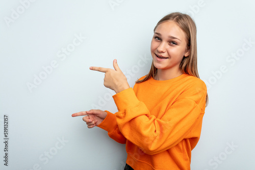 Young caucasian girl isolated on blue background excited pointing with forefingers away.