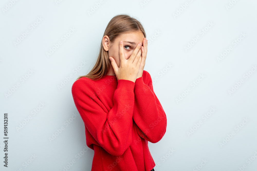 Young caucasian girl isolated on blue background blink through fingers frightened and nervous. Young caucasian girl isolated on blue background blink through fingers frightened and nervous.
