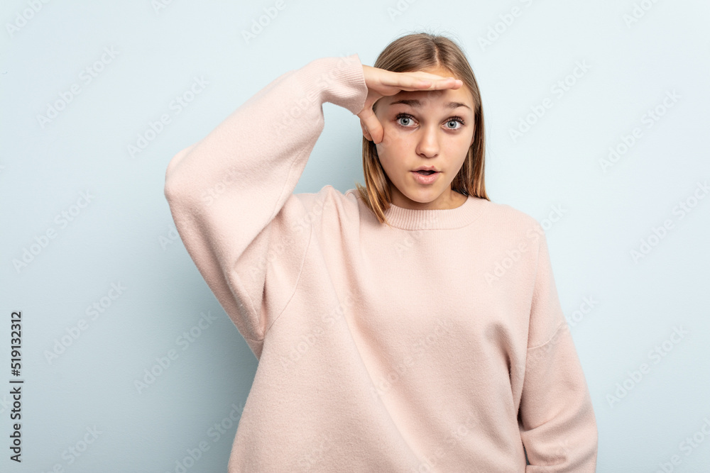 Young caucasian girl isolated on blue background looking far away keeping hand on forehead. Young caucasian girl isolated on blue background looking far away keeping hand on forehead.