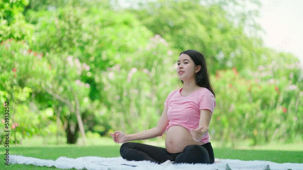 Asia beautiful pregnant woman sitting in the public garden doing yoga or exercise for health. Sport, fitness lifestyle while pregnancy. Workout in summer park doing exercise outdoor in meadow Asia beautiful pregnant woman sitting in the public garden doing yoga or exercise for health. Sport, fitness lifestyle while pregnancy. Workout in summer park doing exercise outdoor in meadow