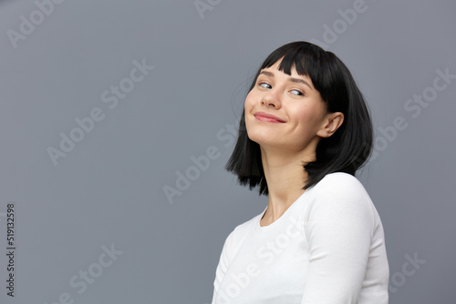 a happy woman stands on a dark background in a tight white T-shirt, slightly tilted her head back, calmly lowering her hands down
