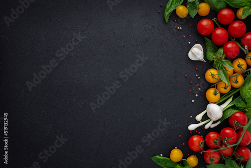 Food background, fresh ripe red and yellow tomatoes, spices and basil leaves, garlic and green onions on a dark background, healthy food concept, copy space, top view