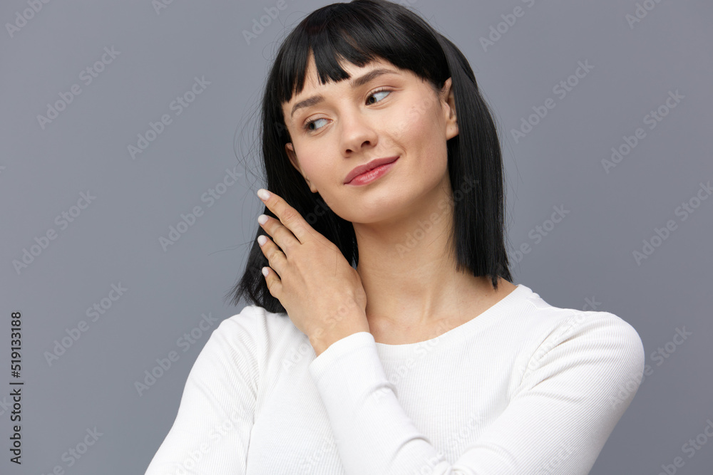 a relaxed woman stands full-face against a dark background in a white tight T-shirt, straightens her hair with her hand, smiling a little, looks away in embarrassment a relaxed woman stands full-face against a dark background in a white tight T-shirt, straightens her hair with her hand, smiling a little, looks away in embarrassment