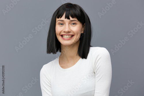 a happy woman is standing on a dark background in a tight white T-shirt, smiling happily with her back slightly bent and her hands relaxed down