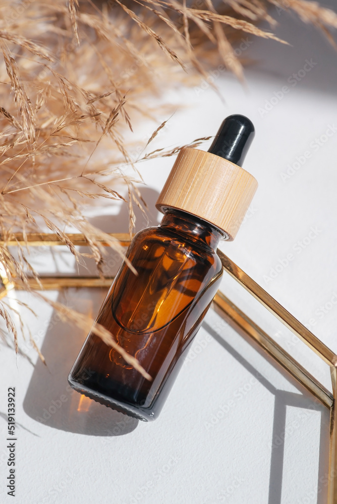 Naklejka premium Amber glass bottle dropper pipette with serum or essential oil on glass plate for product presentation. Skincare cosmetic and with wildflowers. Beauty concept for face body care