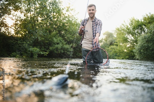 Fototapeta Naklejka Na Ścianę i Meble -  Fisherman catches a trout on the river in summer