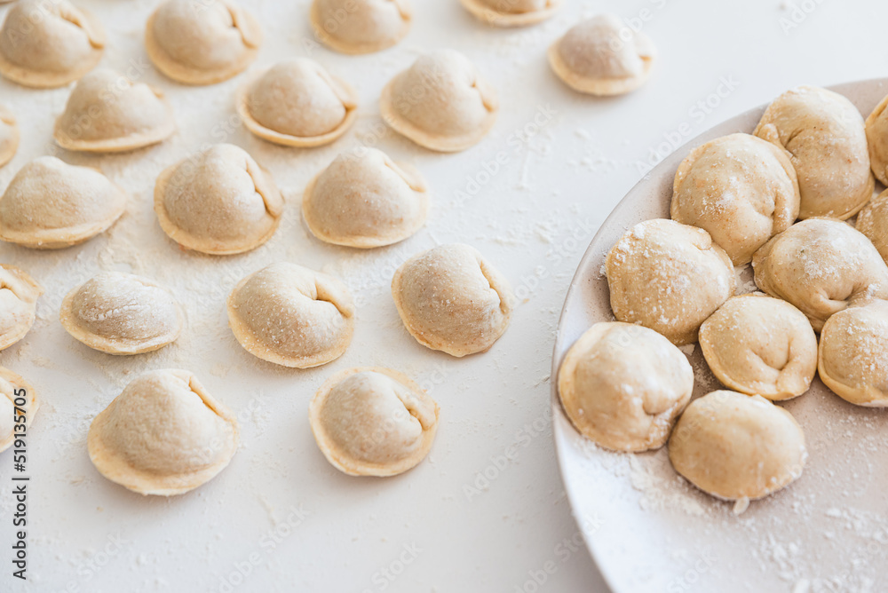 Uncooked homemade pelmeni on white table. Process of making pelmeni, ravioli or dumplings with meat Uncooked homemade pelmeni on white table. Process of making pelmeni, ravioli or dumplings with meat