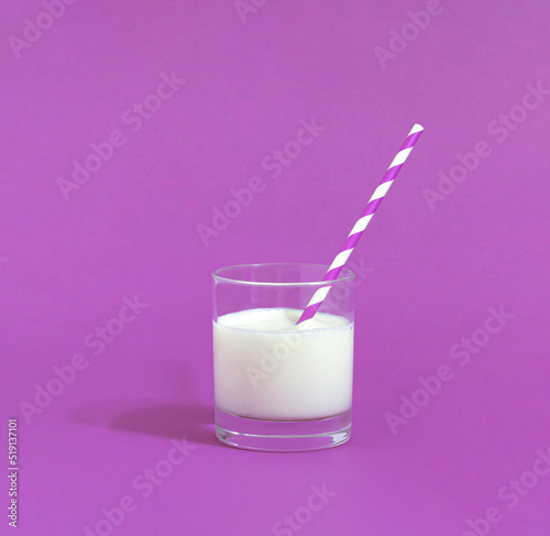 Minimal scene with a glass of cold milk for a pleasant day. White drink with a tube on violet background.