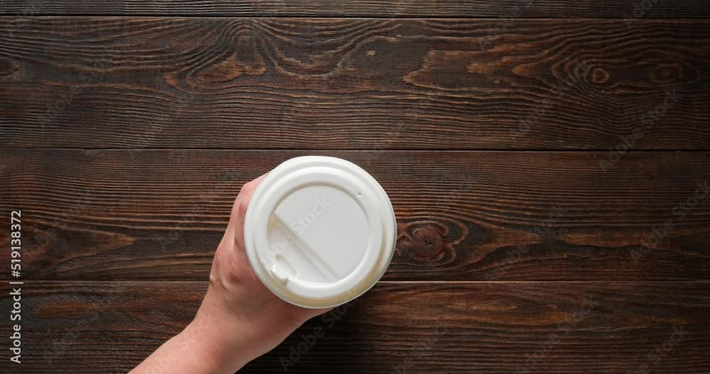 Glass of coffee to go on a wooden brown background. The hand takes a paper cup. 4K stop motion animation