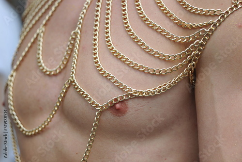 A partial view of a male, muscular chest with golden chains in a row. A creative, modern disguise on the Christopher Street Day in Berlin in the year 2022.