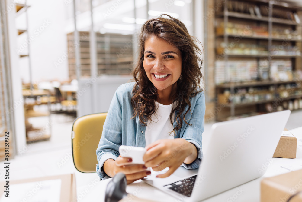Fototapeta premium Successful online store owner using a smartphone in a warehouse