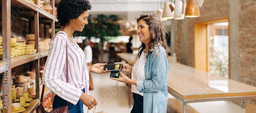Foto Happy store owner receiving an NFC payment from a customer in her shop
